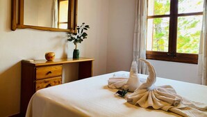 A hotel room with a bed, a wooden dresser, a mirror, a window with curtains, and a plant on the dresser. - Banyols by Rentallorca (Alaro)
