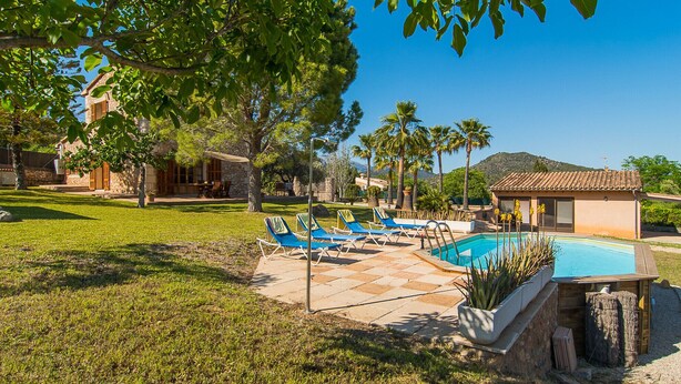 A pool area with lounge chairs, a stone building, and a view of the mountains. - Banyols by Rentallorca (Alaro)