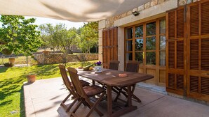 An outdoor patio with a wooden table and chairs, a stone wall, and a view of the garden. - Banyols by Rentallorca (Alaro)