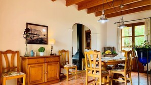 A dining area with wooden furniture, a tiled floor, and a large window with plants. - Banyols by Rentallorca (Alaro)