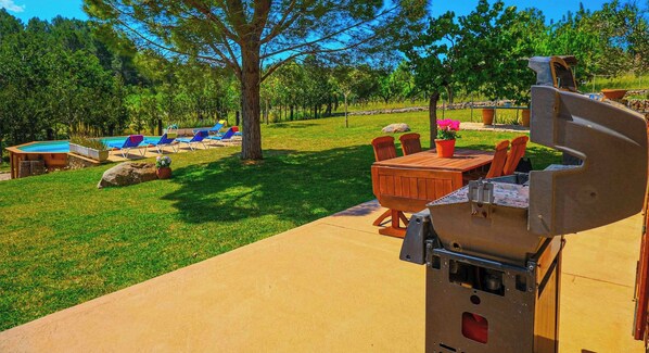A patio with a grill, outdoor seating, and a pool area. - Banyols by Rentallorca (Alaro)