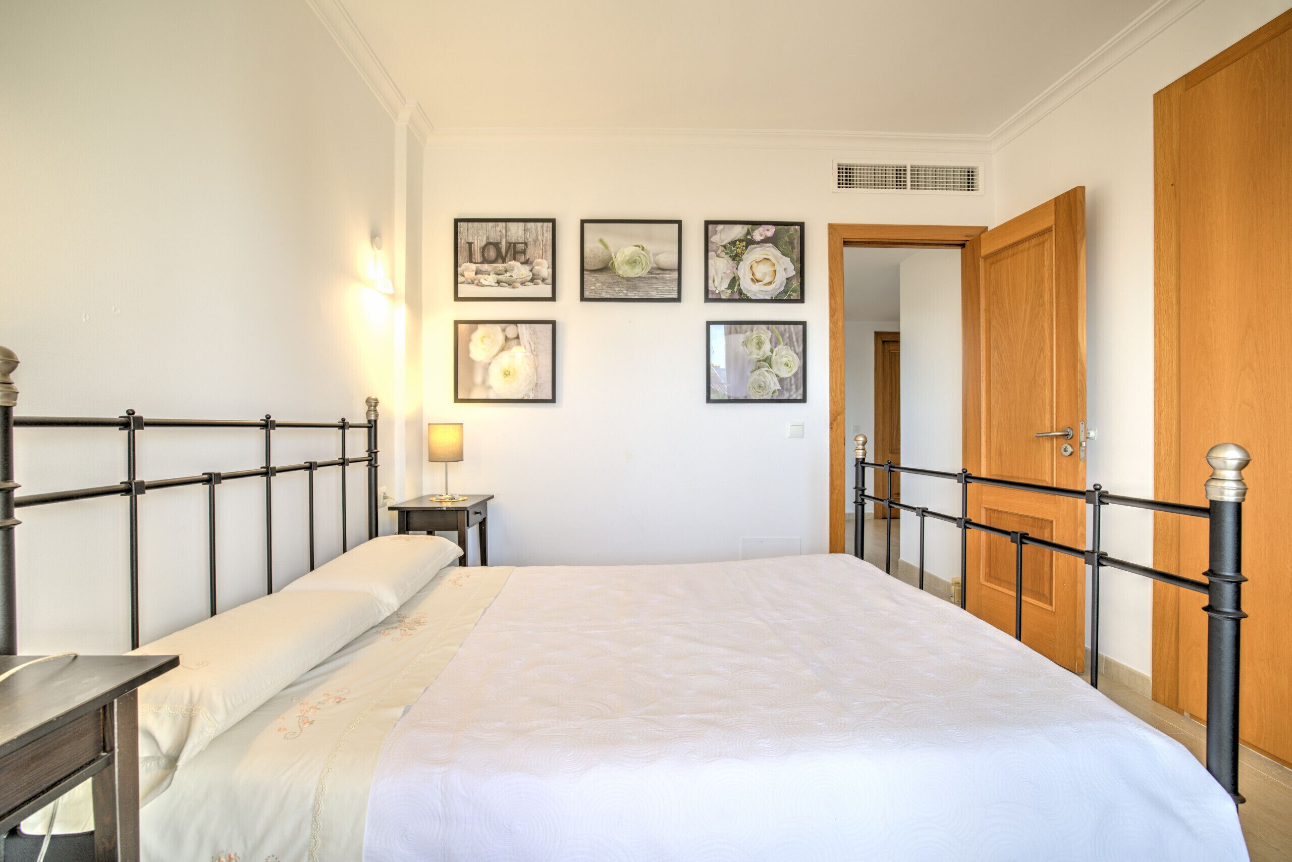 A bedroom with a bed, bedside table, lamp, and framed pictures on the wall.