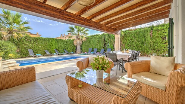 Área externa coberta com piscina, móveis de vime e uma mesa com uma planta.