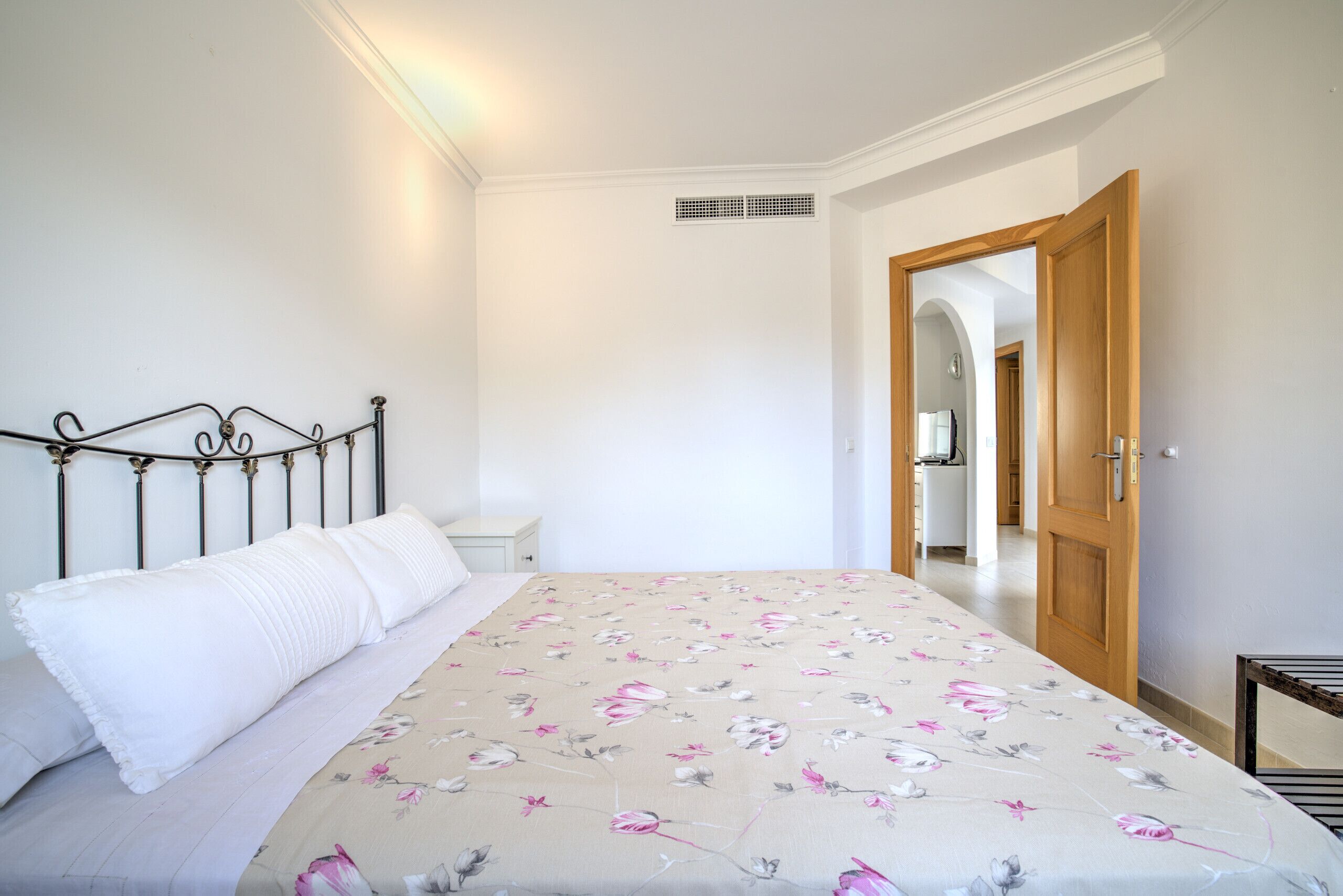 Een slaapkamer met een bed, een nachtkastje, een houten deur en een gang.