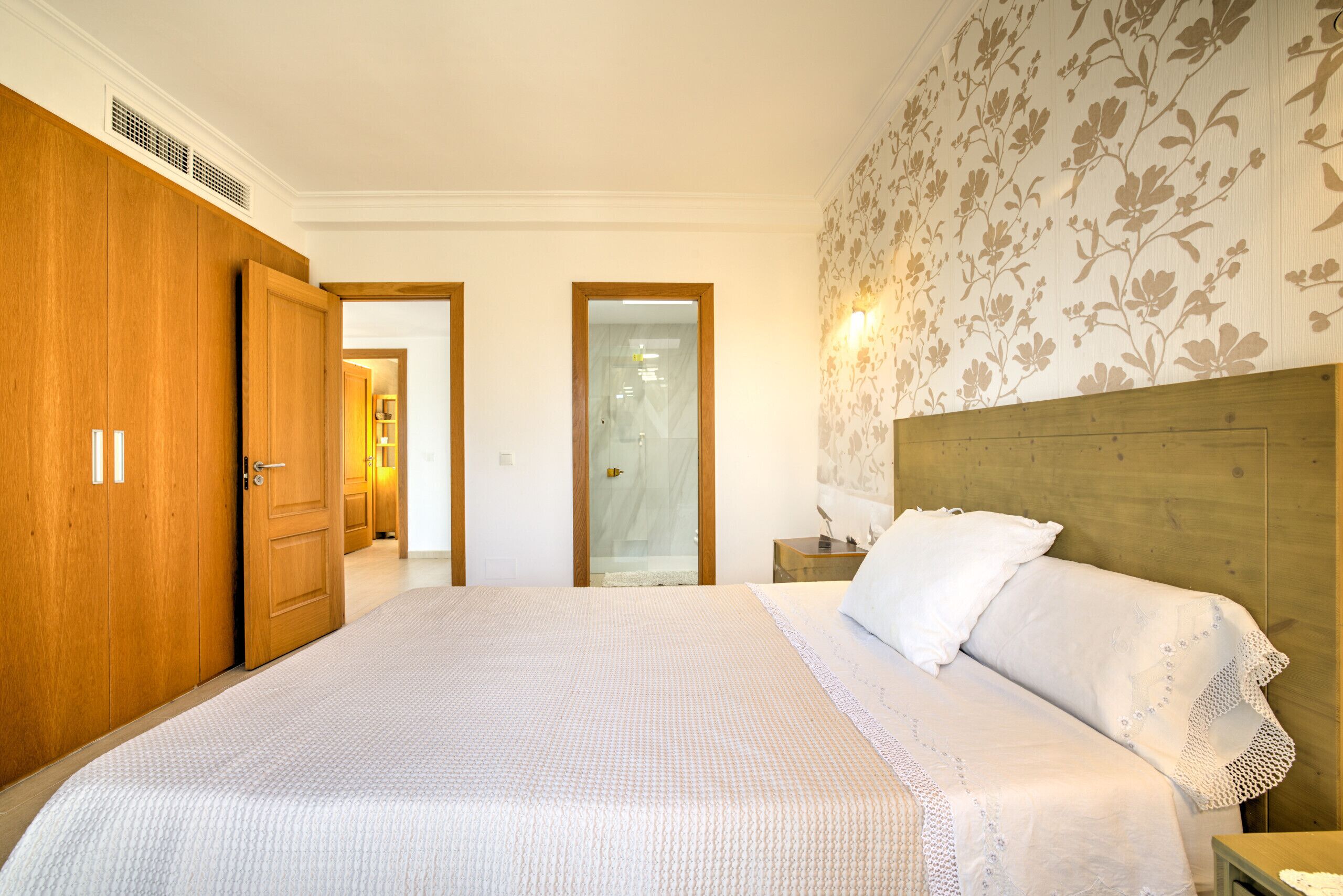A bedroom with a large bed, wooden wardrobe, and a mirror.