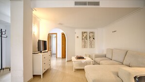 Uma sala de estar moderna com um sofá bege, uma mesa de centro e uma TV em um armário branco.