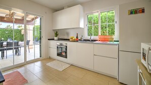 Uma cozinha moderna com armários brancos, forno embutido e uma janela ampla com vista para o verde.