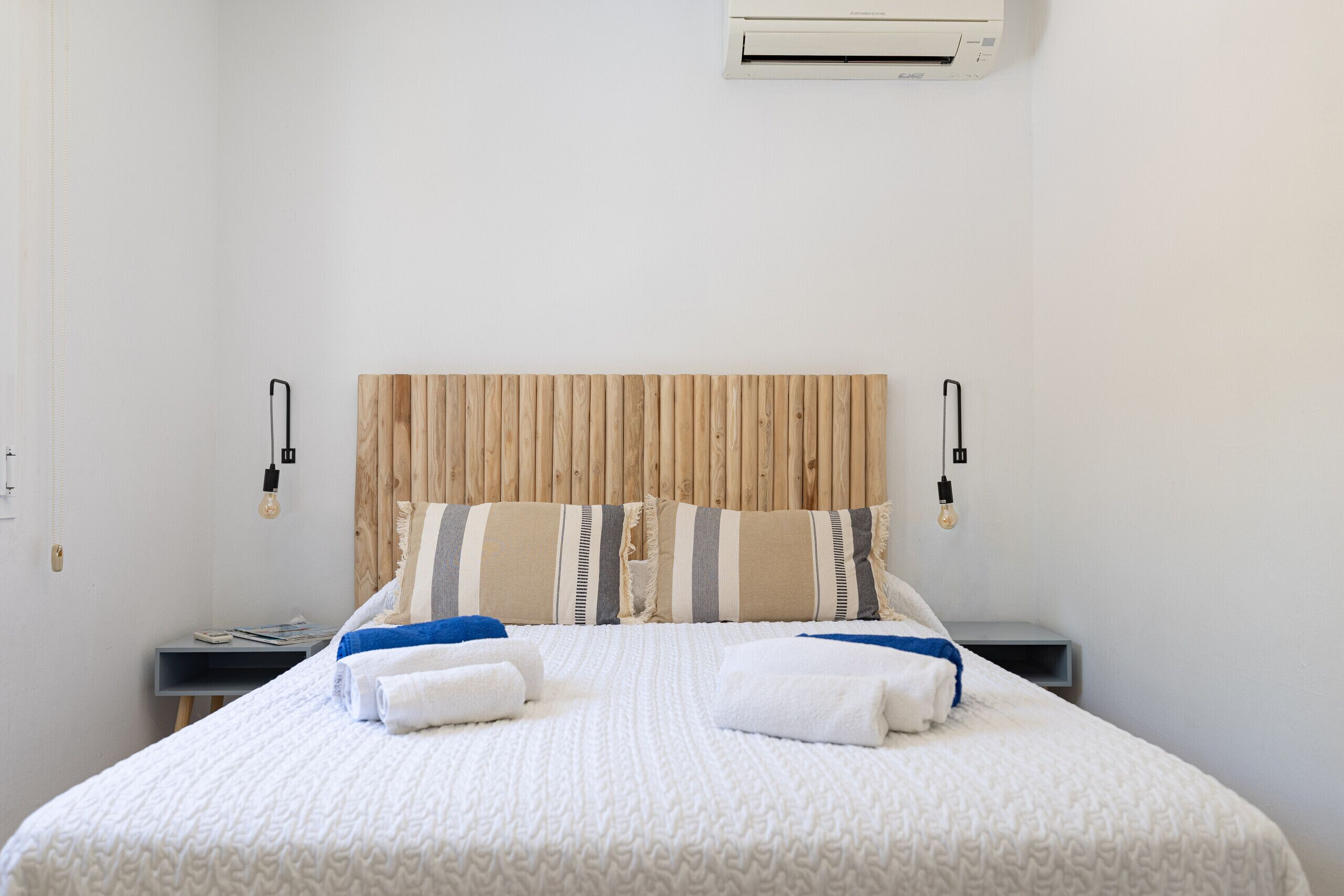 A neatly made bed with a wooden headboard, two bedside tables, and a wall-mounted air conditioner.