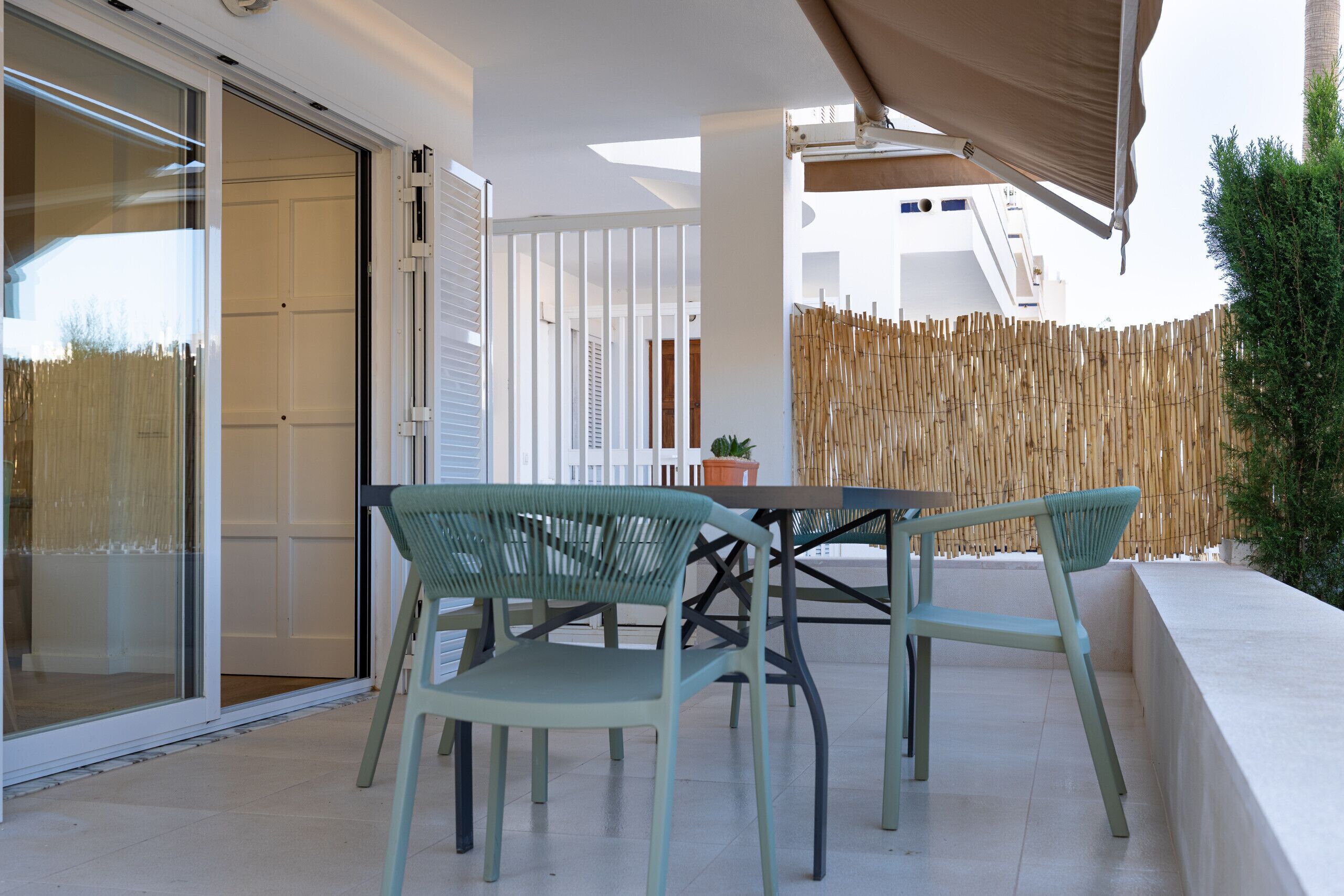A patio with a table and chairs, a sliding glass door, and a bamboo fence.