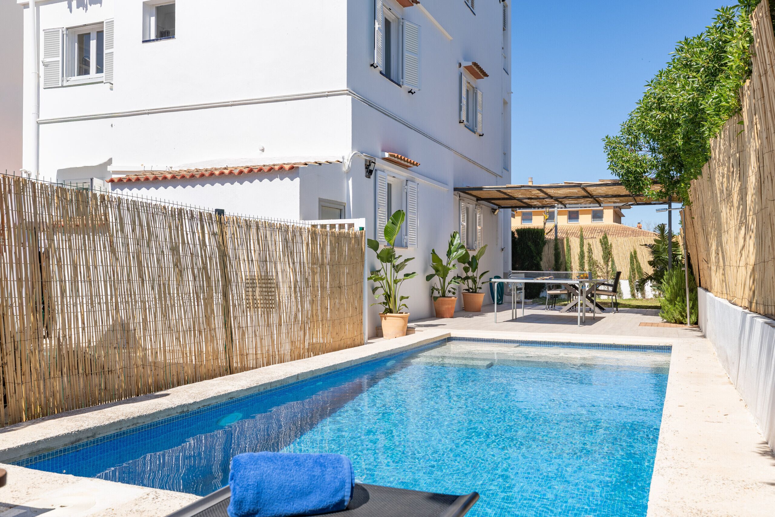 A swimming pool with a bamboo fence, potted plants, and outdoor furniture.