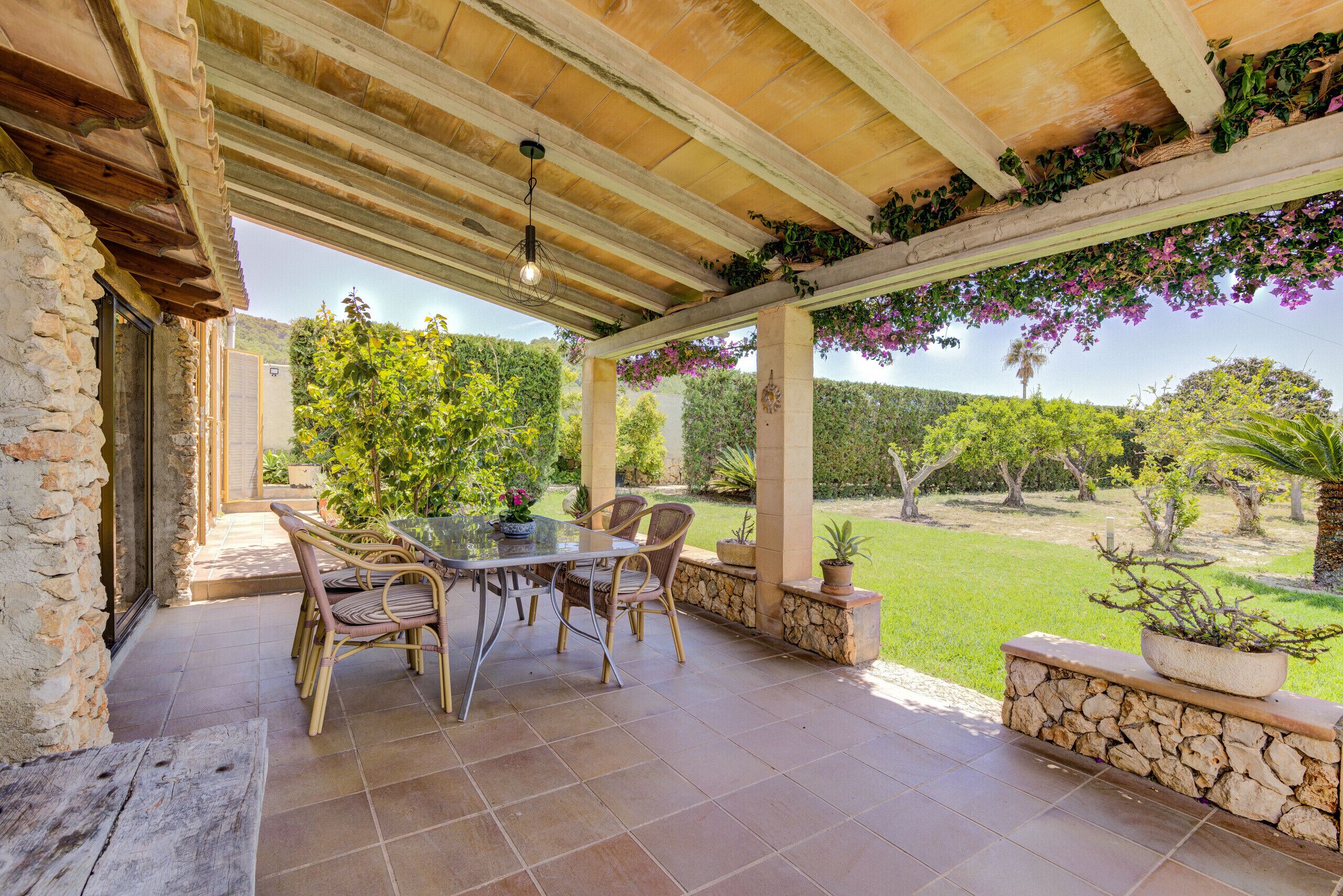 A covered patio with a table and chairs, stone walls, and potted plants.