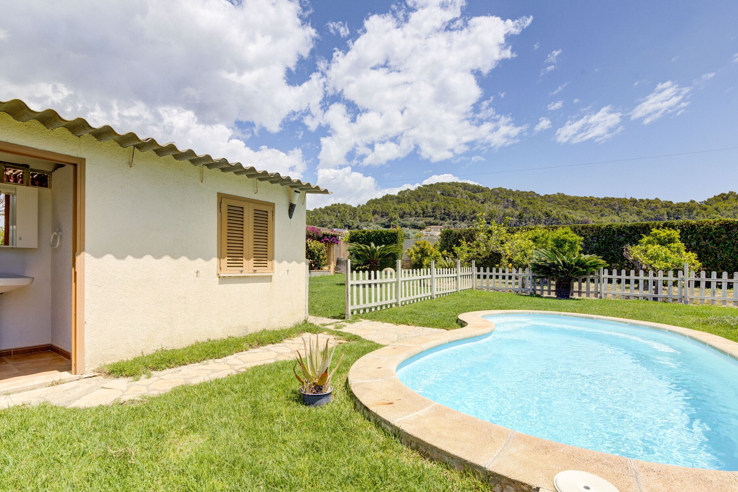 A house with a swimming pool, a white picket fence, and a mountain in the background.