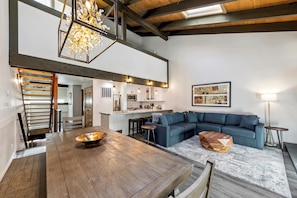 A spacious living area with a wooden dining table, a blue sectional sofa, and a kitchen in the background.