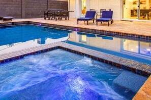 A swimming pool with a hot tub, lounge chairs, and a table.