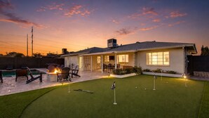 Una casa con patio trasero que incluye piscina, mobiliario exterior y campo de golfito.