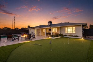 A house with a backyard featuring a pool, outdoor seating, and a putting green.