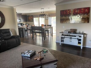 A living room with a fireplace, a dining area with a table and chairs, a kitchen with cabinets and appliances, and a large painting on the wall.