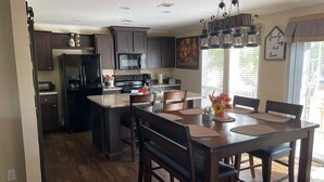 Une cuisine moderne avec des meubles de couleur bois foncé, un îlot central et un coin repas comprenant une grande table et des chaises.