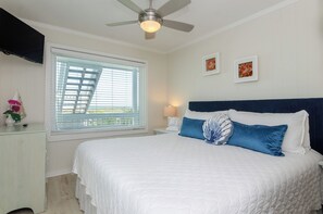A bedroom with a bed, a ceiling fan, a window with blinds, and two framed pictures on the wall.