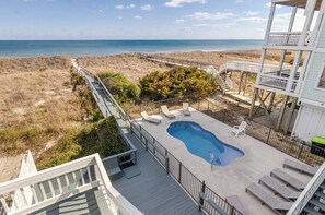 Ein Poolbereich mit Blick auf Strand und Meer, umgeben von einer Terrasse und Liegestühlen.