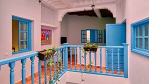 Un interior con varios niveles, una barandilla azul, piso de baldosas y techo con vigas a la vista.
