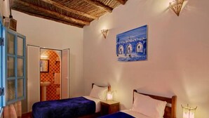 Una habitación con dos camas, una puerta azul y un cuadro de arcos en la pared.