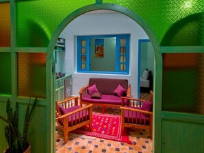 Una habitación acogedora con sofá y sillones, un tapete estampado y una ventana con persianas azules.