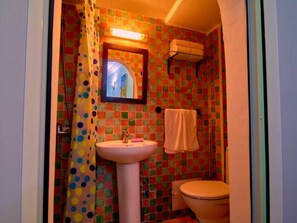 Un baño con una pared de mosaicos de colores, un lavamanos blanco, un inodoro y una cortina de ducha con estampado de lunares.
