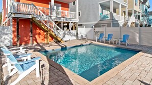 A swimming pool with a wooden deck, a covered area with a staircase, and a building with multiple balconies. - Walk to Beach 6BR Home w/ Private Pool & Beachside Porches (Surfside Beach)