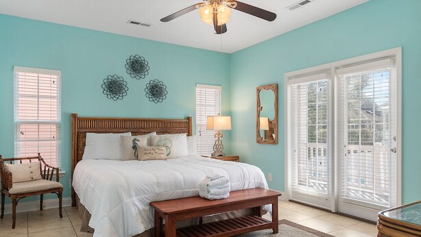 A bedroom with a bed, a chair, a bench, a ceiling fan, and a large window with blinds. - Walk to Beach 6BR Home w/ Private Pool & Beachside Porches (Surfside Beach)