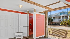 A covered porch with a swing, a white door, and a red wall. - Walk to Beach 6BR Home w/ Private Pool & Beachside Porches (Surfside Beach)