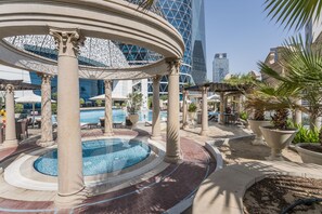 A pool area with a circular fountain, palm trees, and modern buildings in the background.
