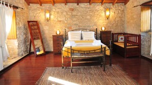 Ein Schlafzimmer mit Steinsandsteinwand, Holzboden und einem Bett mit Metallgestell, Nachttischen und einem Spiegel.