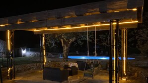 Ein Patio im Freien mit Steinboden, einer Holzpergola mit Lichterketten, einem Pool und Gartenmöbeln.