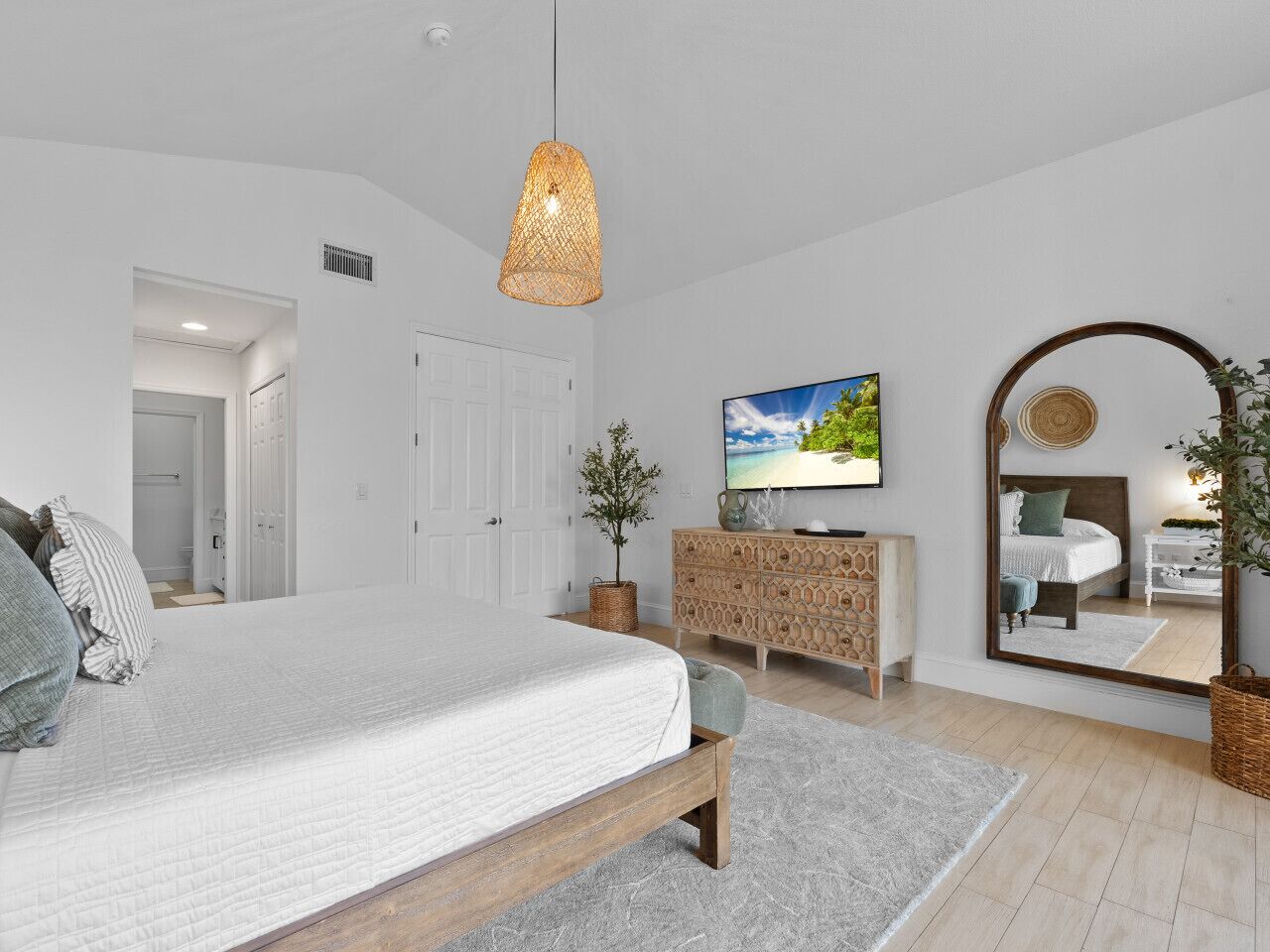 A bedroom with a bed, a television, a dresser, a mirror, and a plant.