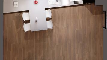 Vista cenital de una habitación de hotel moderna con suelo de madera, un sofá, una cama, un baño con ducha y lavabo, y una mesita con un jarrón.