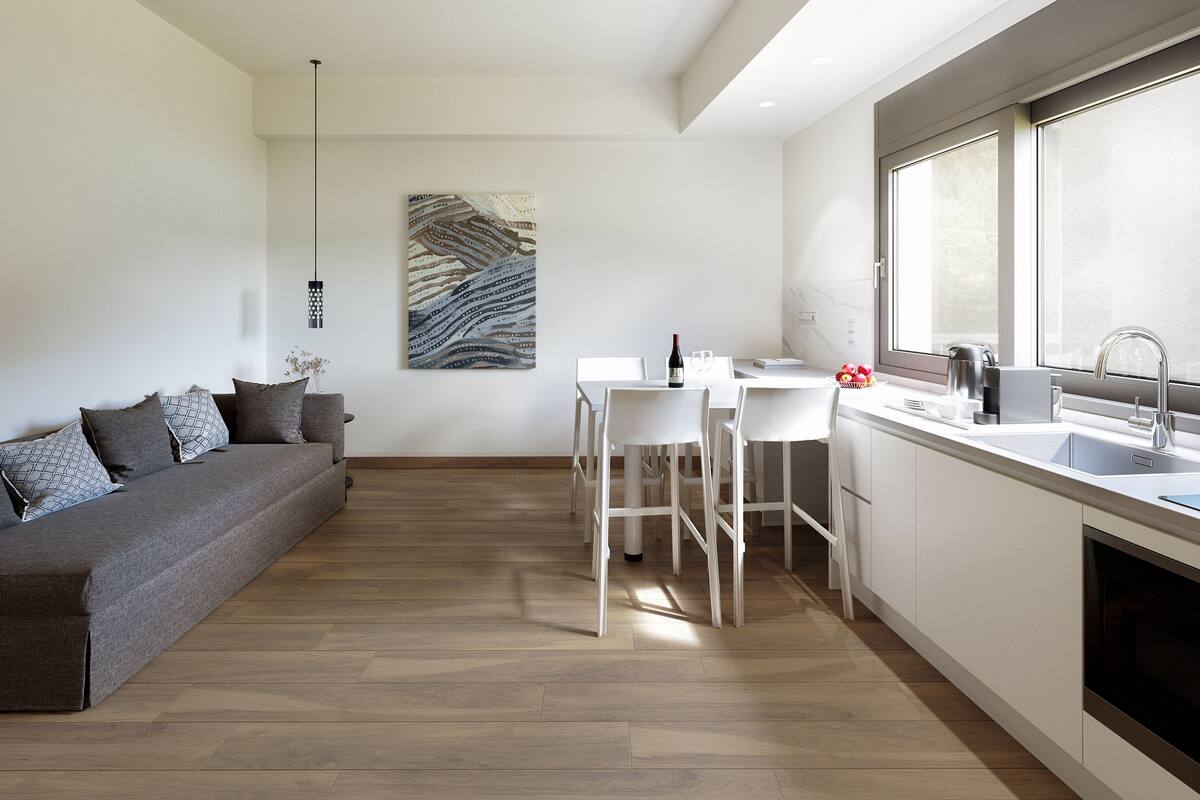 Een moderne keuken met witte kasten, een eethoek met witte stoelen, en een grijze bank met gestreepte kussens.