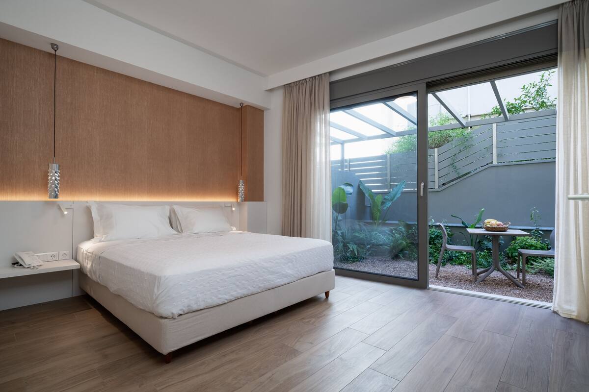 Een moderne slaapkamer met een groot bed, een nachtkastje met een telefoon, en uitzicht op een buitenste tuin door een schuifglazen deur.