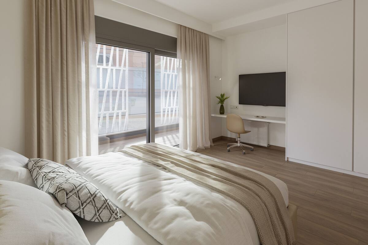 Een moderne hotelkamer met een groot bed, een bureau met stoel, een flatscreen televisie en een groot raam met gordijnen.
