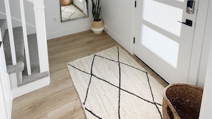 A hallway with a white door, a mirror, a framed picture, a potted plant, and a geometric rug. - Luxury Downtown Spacious 3 bedroom New Modern Townhome (Provo)