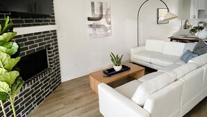 A modern living room with a white sofa, a wooden coffee table, a black fireplace, and a potted plant. - Luxury Downtown Spacious 3 bedroom New Modern Townhome (Provo)