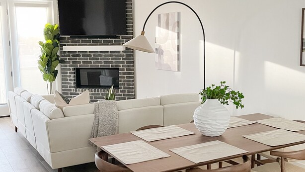 A modern living room with a fireplace, a sofa, a dining table with chairs, and a TV mounted on the wall. - Luxury Downtown Spacious 3 bedroom New Modern Townhome (Provo)