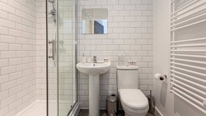 Ein modernes Badezimmer mit weißen Fliesen im U-Bahn-Stil, einer Glasdusche, einem Standwaschbecken, einer Toilette und einem Heizkörper.
