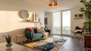A modern living room with a sofa, coffee table, and a large window. - Bright Contemporary 2BED Apartment by Old Trafford (Manchester)