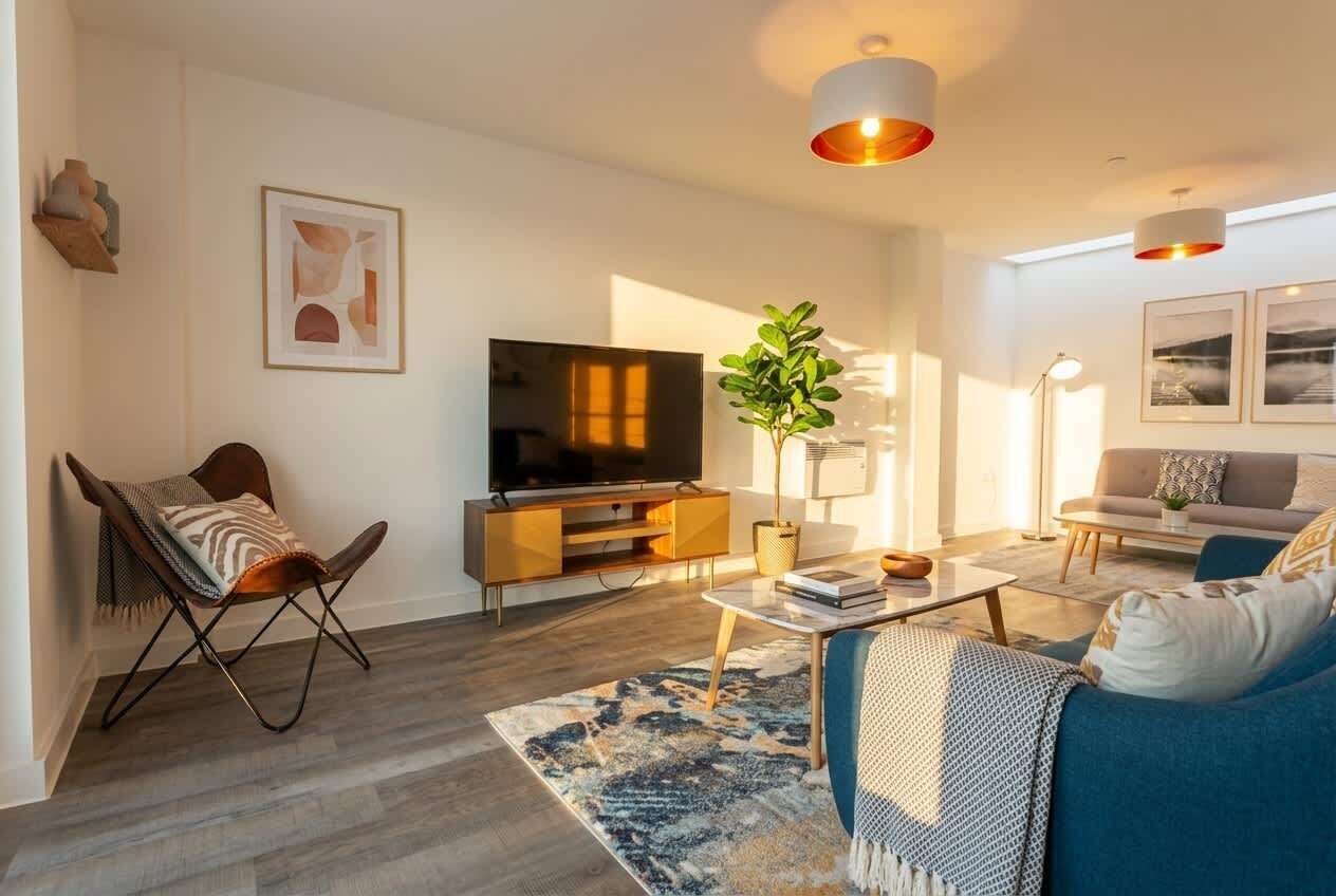 A modern living room with a flat-screen TV, a blue sofa, a coffee table, and a patterned rug.