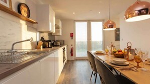 A modern kitchen with a central island, a dining area with a table set for two, and a large window providing natural light. - Bright Contemporary 2BED Apartment by Old Trafford (Manchester)