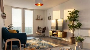 A modern living room with a sofa, coffee table, TV, and potted plants. - Bright Contemporary 2BED Apartment by Old Trafford (Manchester)