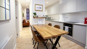 Une cuisine moderne avec des meubles blancs, une table à manger en bois et une bouilloire rouge.