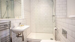 Une salle de bain moderne avec des carreaux blancs, une douche en verre, un lavabo avec un miroir et un porte-serviettes.