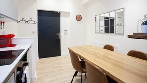 Une cuisine moderne avec des meubles blancs, une porte noire, une table à manger en bois avec quatre chaises et un miroir au-dessus de la table.